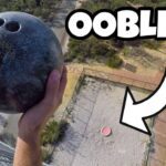 Person gripping a bowling ball high above a fenced courtyard, captured from a balcony; bold thumbnail text says OOBLECK.