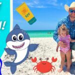Family with a dad and two kids on a sunny beach, cartoon shark and crab decorations, and a blue 'Visit the Beach!' banner in the background.