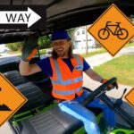 Safety-vested worker driving a small vehicle with multiple orange road-sign overlays (construction, cyclist, stop, traffic light, one-way).